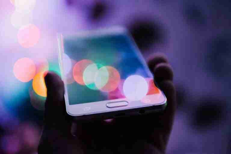 A person holding an Argos unlocked mobile phones smartphone with a glowing screen, set against a backdrop of colorful bokeh lights.